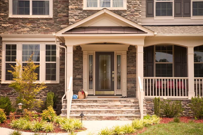 Brown front door with decorative windows and metal trim on stone house porch